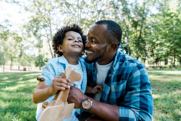 Happy father and son hugging outside, while holding a toy plane.
