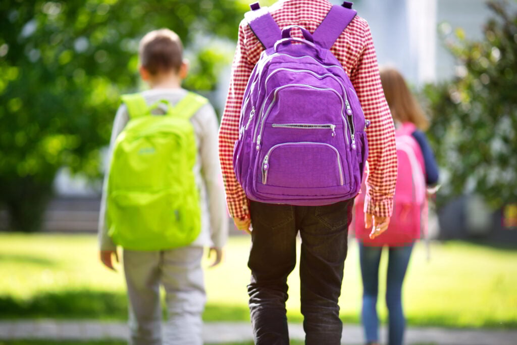 Children with rucksacks standing in the park near school