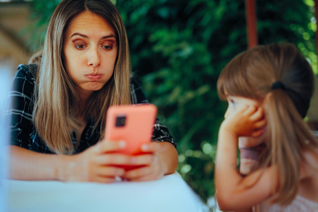 Mom Checking her Phone while Sitting next to her Daughter