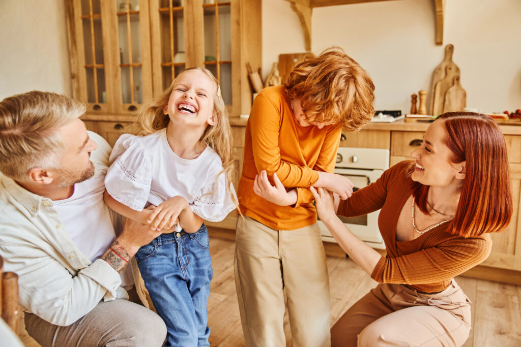 excited parents tickling laughing children and having fun in modern kitchen at home, bonding