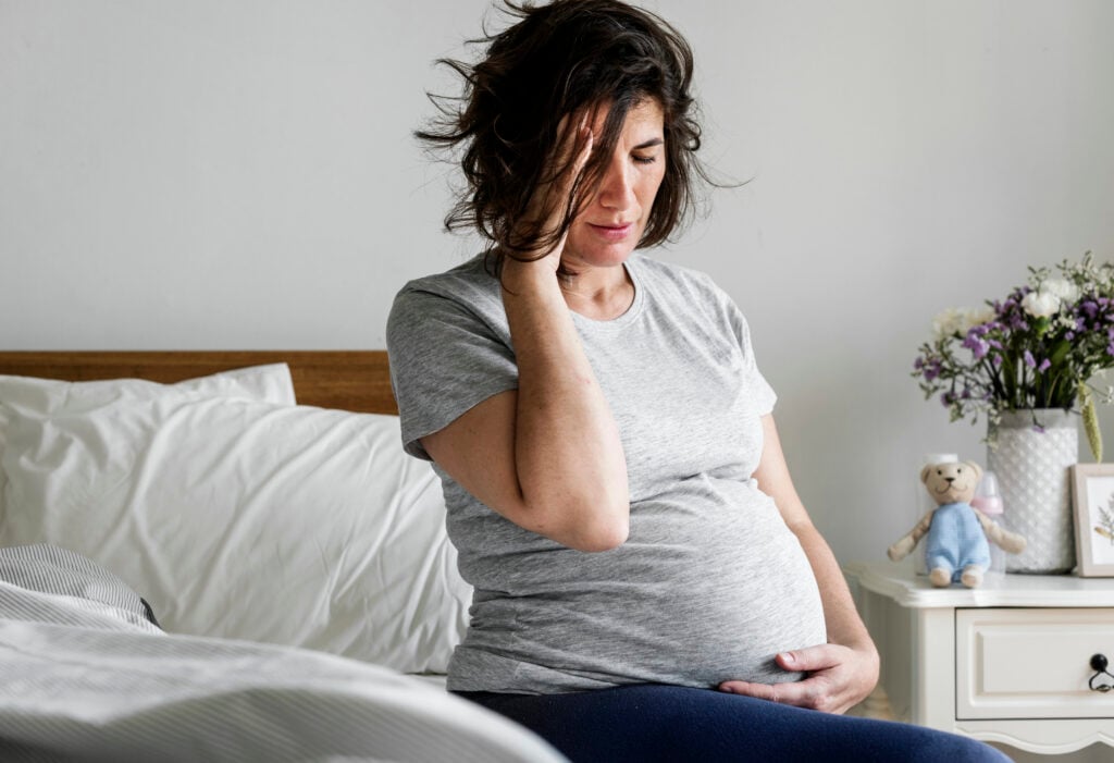 Pregnant woman with a headache on bed