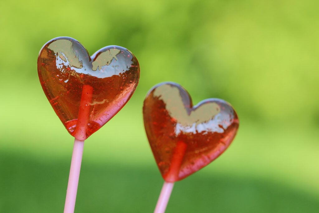 Red lollipops in heart shape, on fresh green grass, in the garde