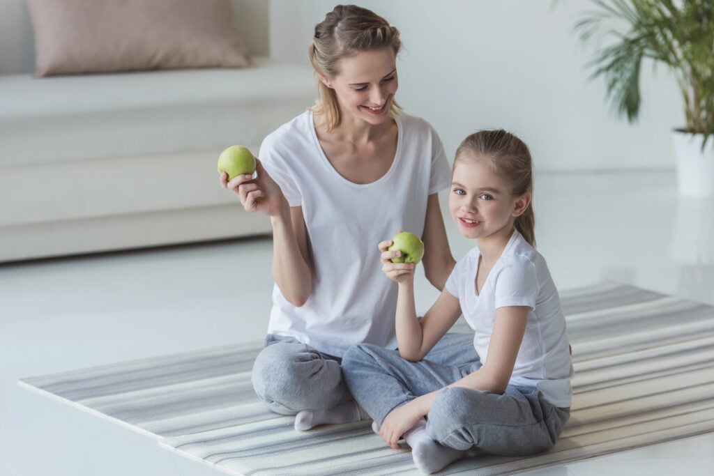 happy mother and daughter eating apples on floor