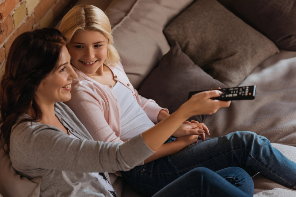 Mom and daughter smiling happily while watching a movie together. 