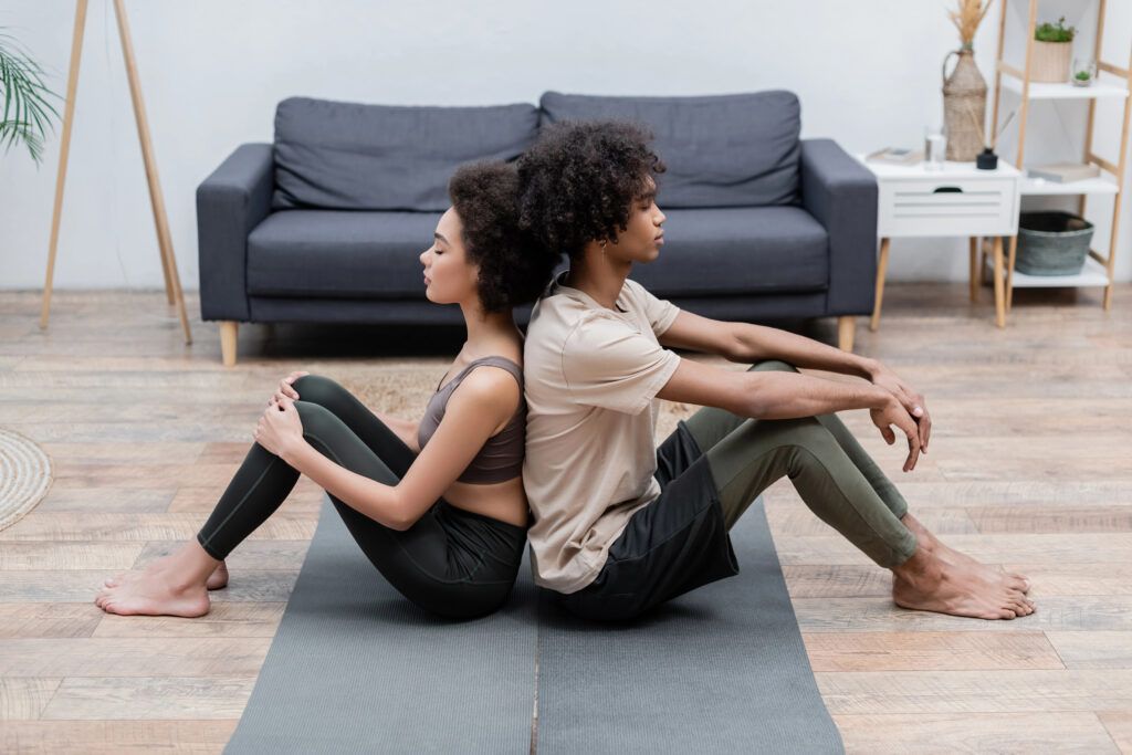 Side view of young african american couple meditating back to back on yoga mats at home
