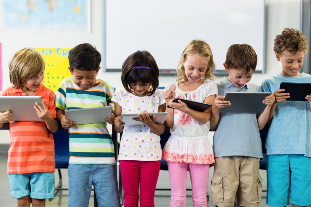 Smiling schoolchildren using digital tablet