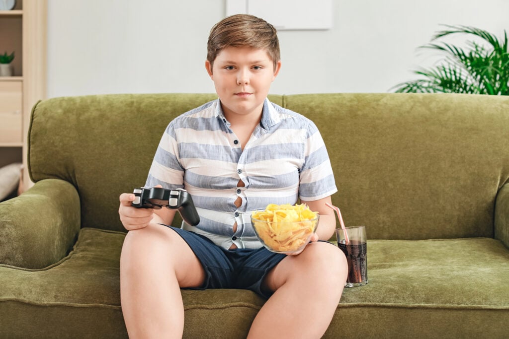 Overweight boy with chips playing video game at home