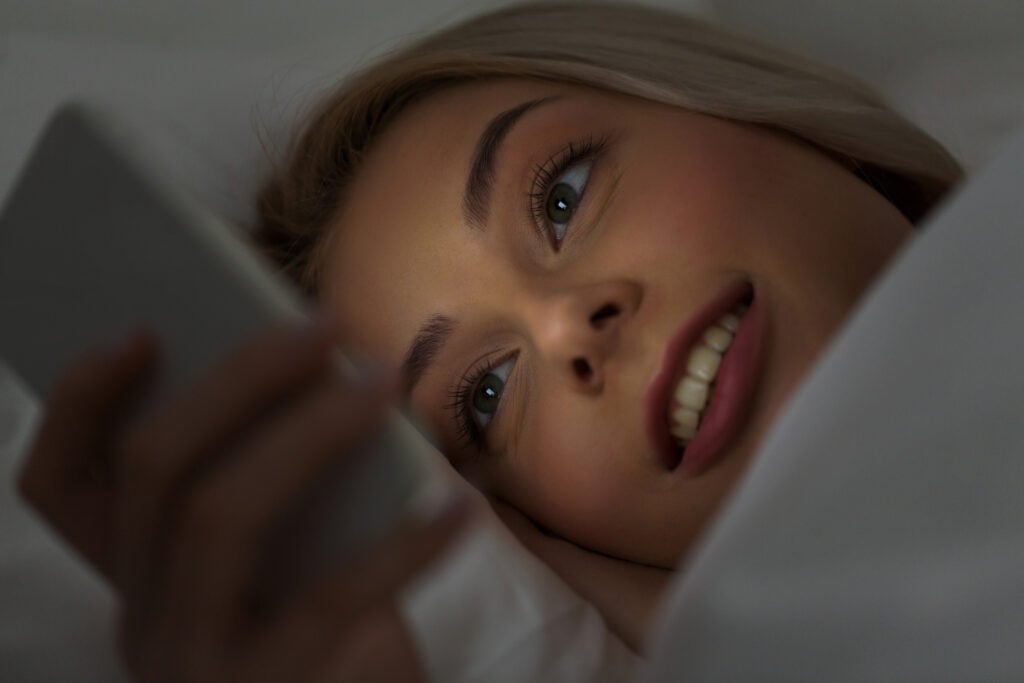 young woman with smartphone in bed at night