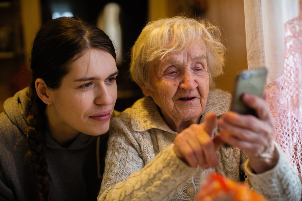 An old lady looks at a smartphone, with his adult granddaughter.