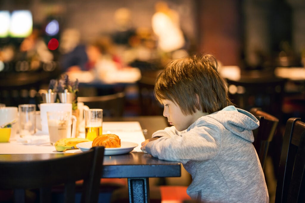 Little boy, child, enjoying breakfast in hotel restaurant, eating croissant