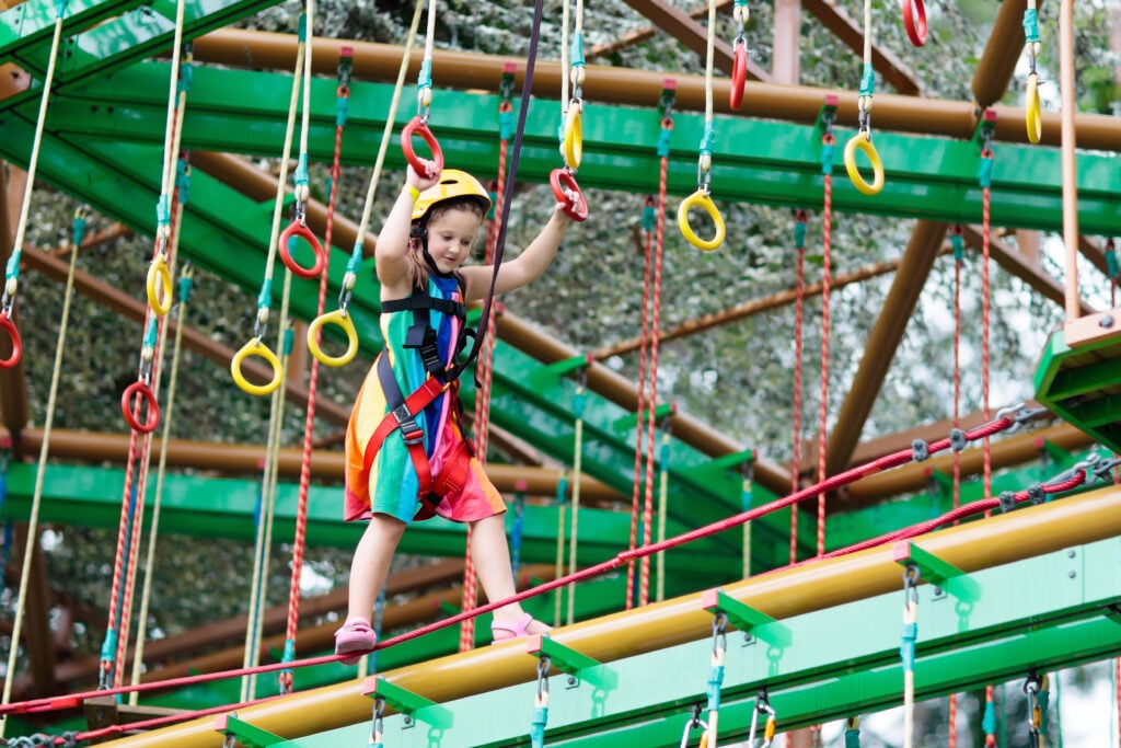 Child in adventure park. Kids climbing rope trail.