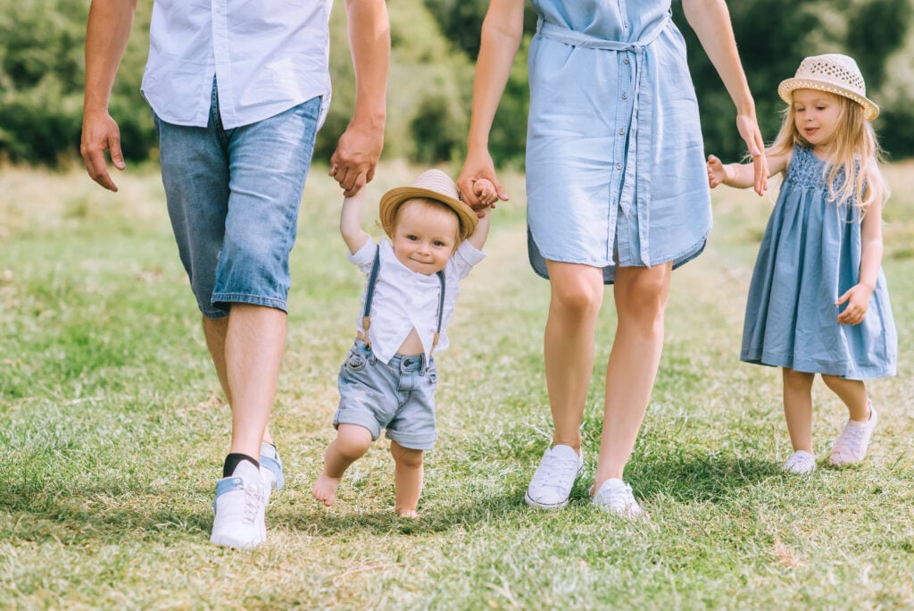 parents holding hands with children and walking on green feild together