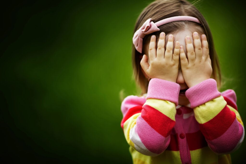 little girl is playing hide-and-seek hiding face
