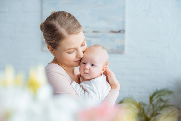 selective focus of happy young mother hugging adorable baby at home
