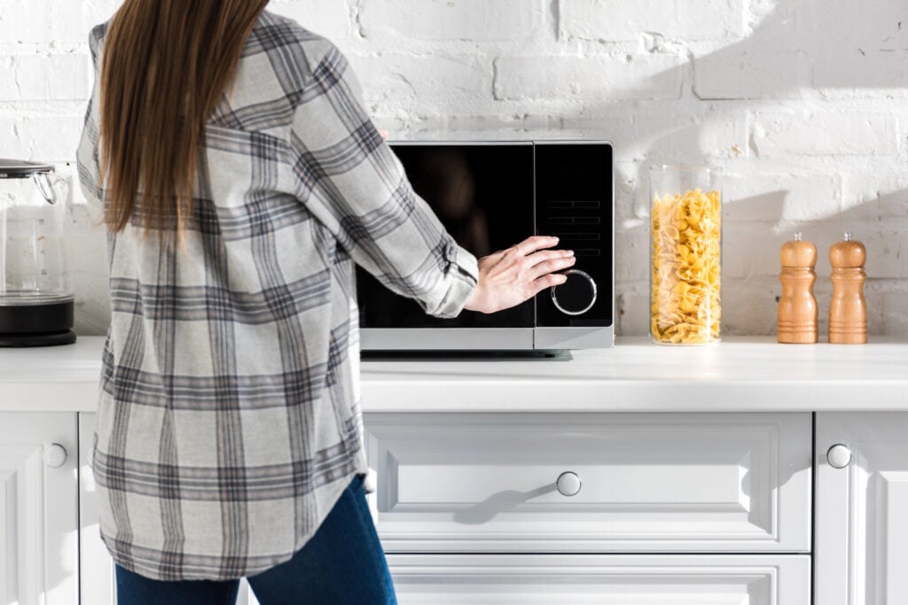 cropped view of woman in shirt using microwave in kitchen