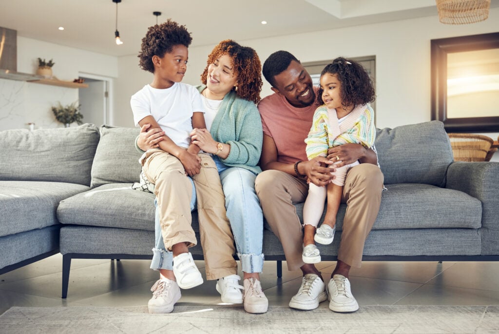 Black family, love and bond on a sofa, happy and smile while talking and enjoying a morning in their home. Relax, children and parents on couch together, embrace and loving in living room on weekend.