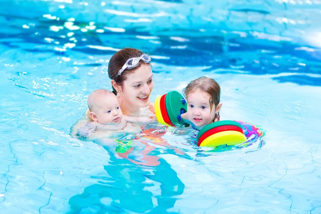 Young active mother having fun in a swimming pool with two kids