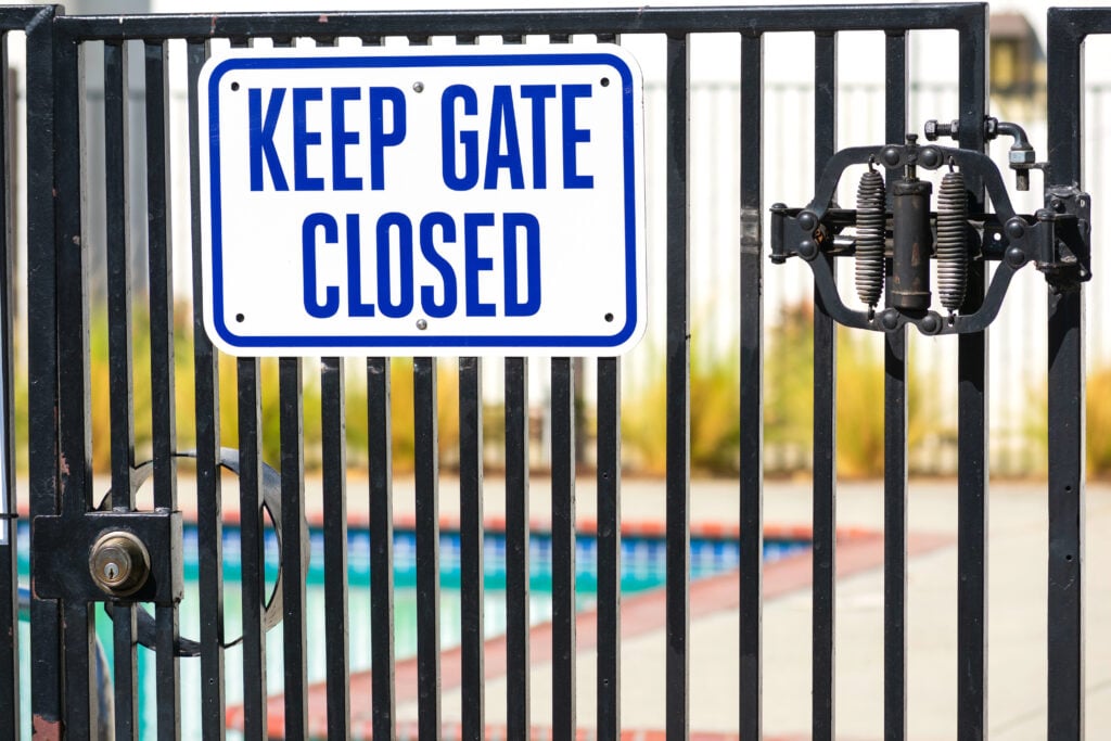 Keep Gate Closed warning sign on the locked entrance door to outdoor pool to remind people to keep the swimming pool gate closed.