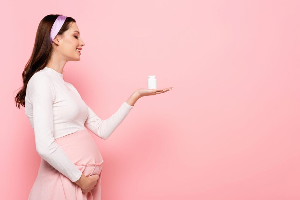 happy young pretty pregnant woman with vitamins isolated on pink