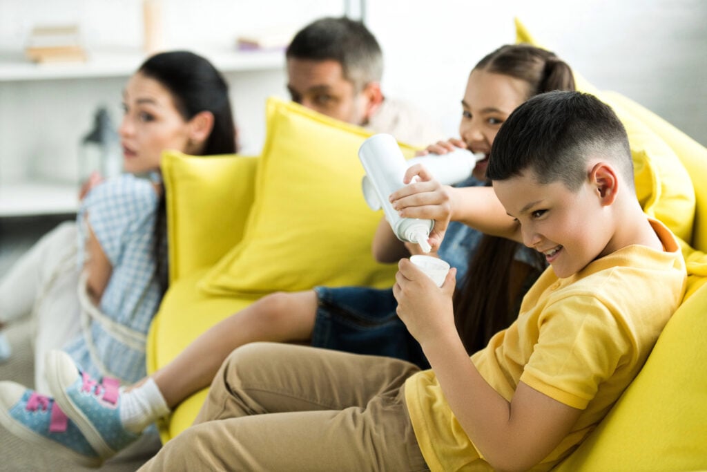 tied parents sitting near sofa and children eating sweets at home, parenthood concept