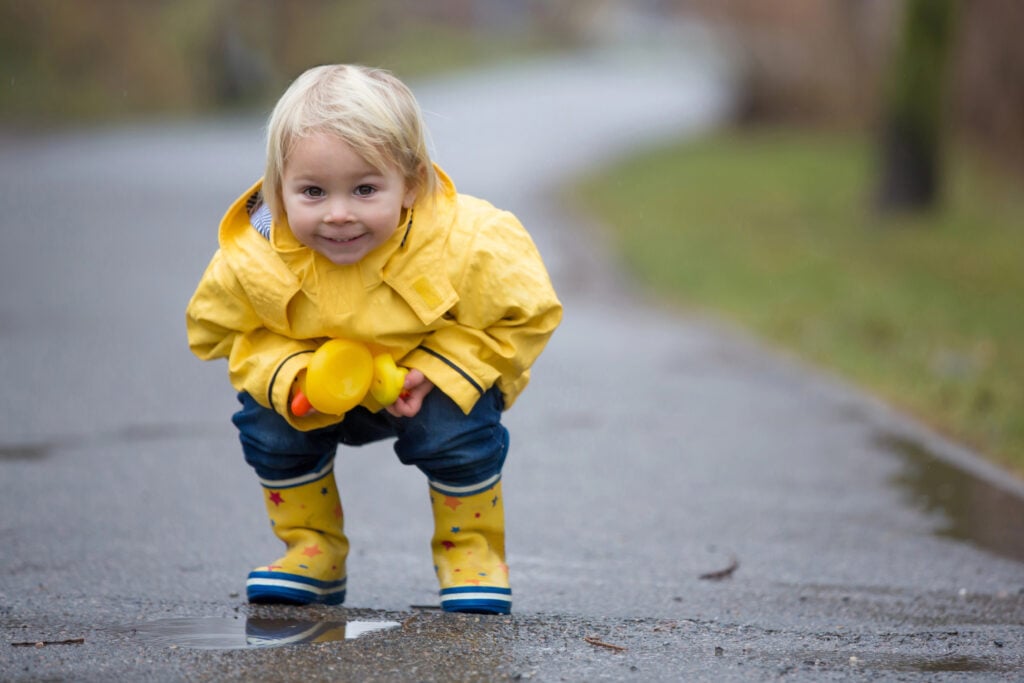 Beautiful funny blonde toddler boy with rubber ducks and colorfu