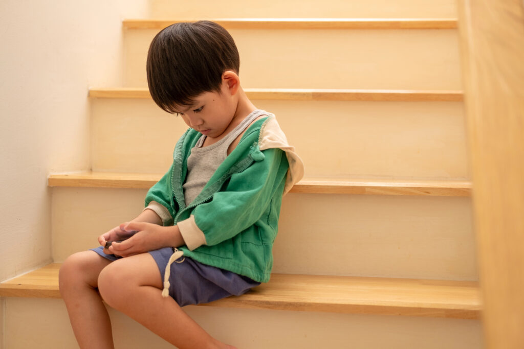 A boy who was scolded by his mother secretly came to play on the phone on the stairs.