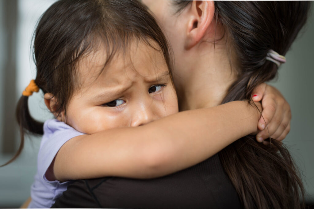 A sad little girl hugging her parent to feel safe, tearful.