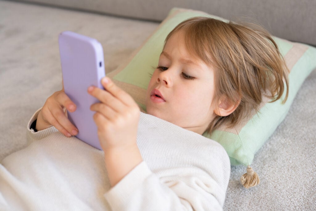 Adorable caucasian boy using smartphone sitting on sofa at home