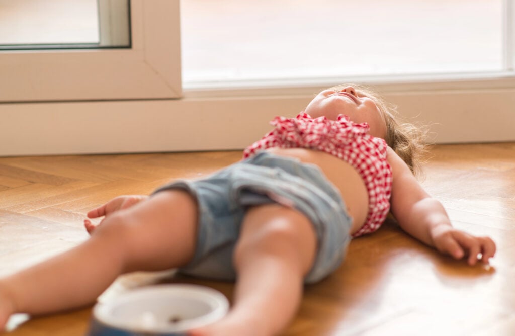 Beautiful blond child crying and shouting with tantrum laying on the floor at home.