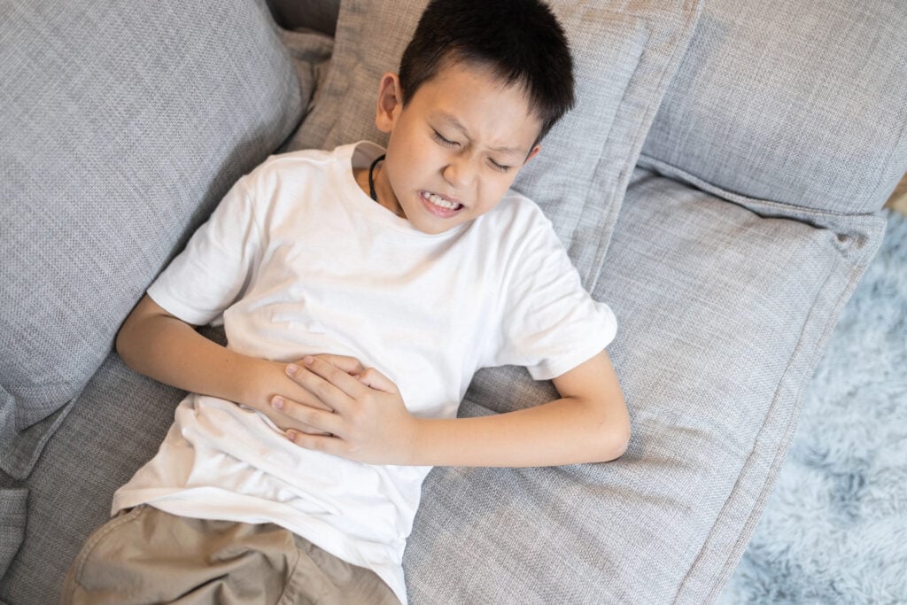Sick asian child boy suffering from stomachache,holding his belly,severe abdomen pain,appendix becomes inflamed and painful,abdominal disease,acute appendicitis,medical emergency,health care concept