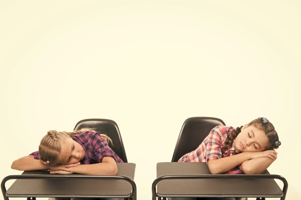 Surviving a boring lesson. Cute school children sleeping at school desks. Little schoolgirls got tired at lesson in primary school. Small girls doing a nap during lesson. Most boring lesson ever