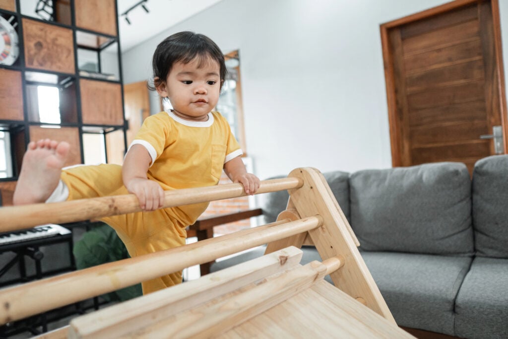 baby trying to raise its legs while climbing on the triangle toy pikler