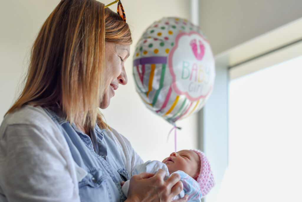 woman cuddling newborn baby granddaughter in hospital