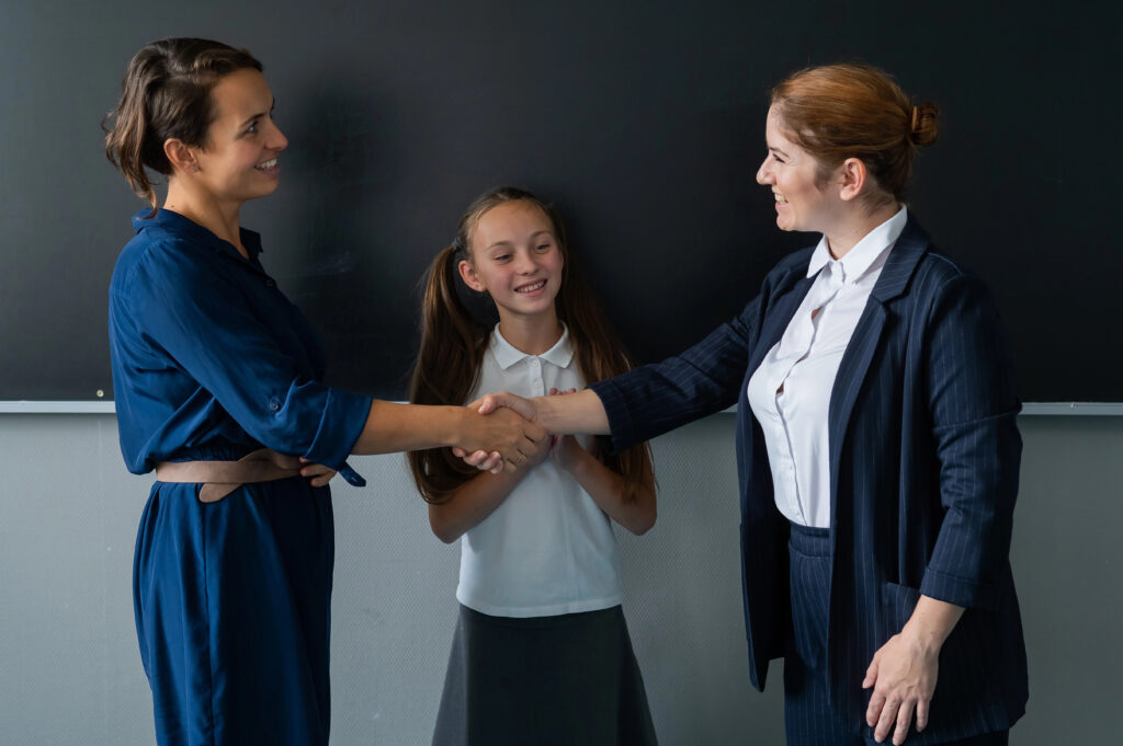 The teacher shakes hands with the mother of the schoolgirl standing at the blackboard