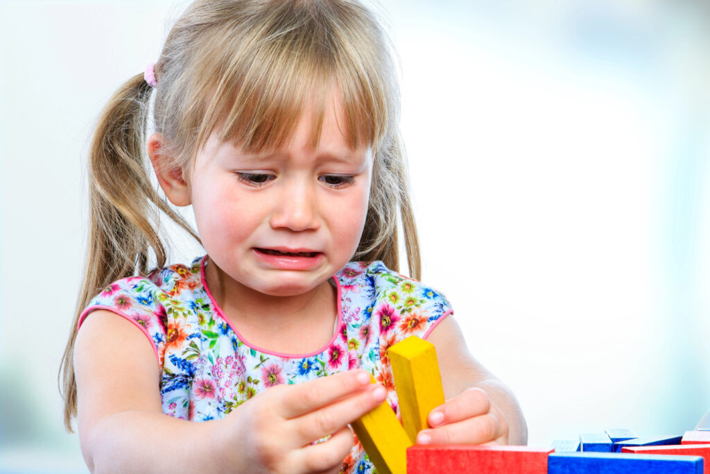 Unhappy little girl playing with wooden blocks.