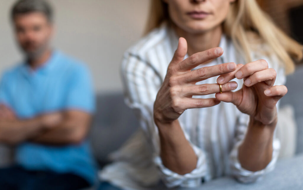 Woman taking off her ring with her ex-partner in the background. 