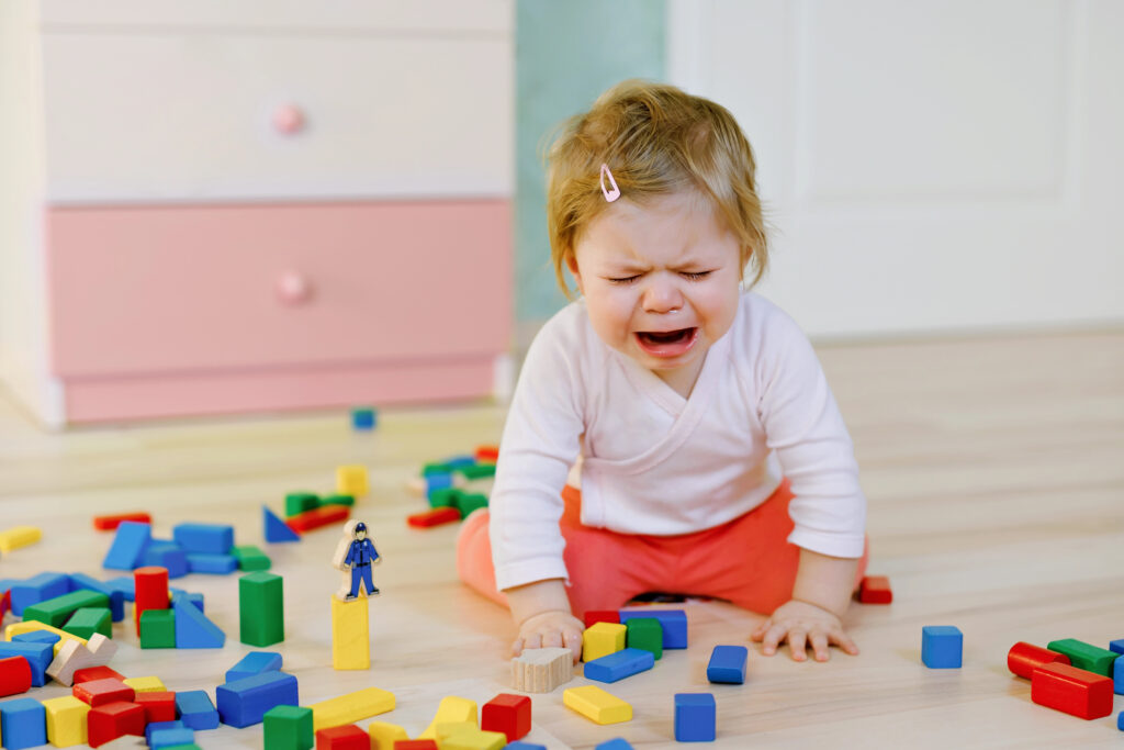 Child crying in her room surrounded by toys.
