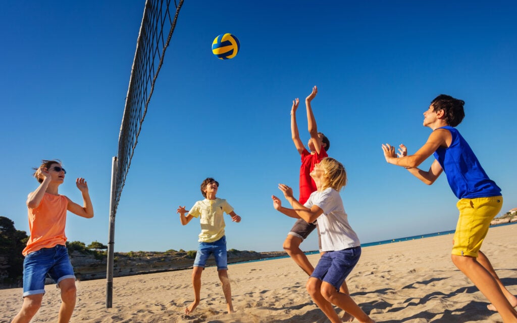 Low-angle shot of teenage boys playing volleyball on the beach in summer