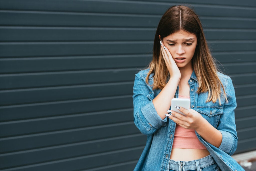 Worried teenager using smartphone near building outdoors