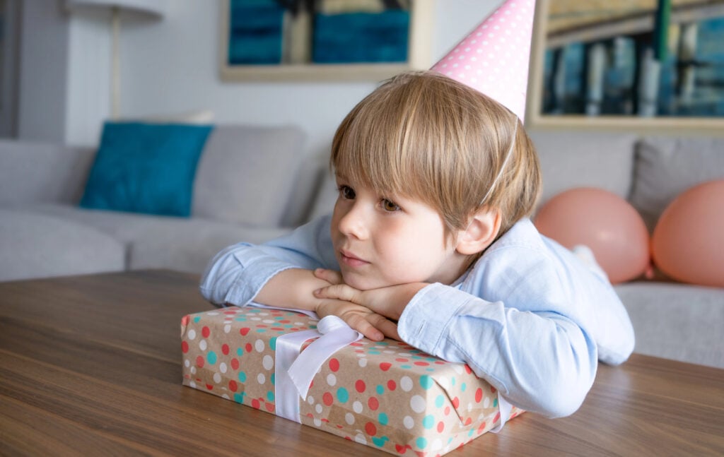 Close up portrait of happy little child boy in birthday hat with a big gift box sitting in living room