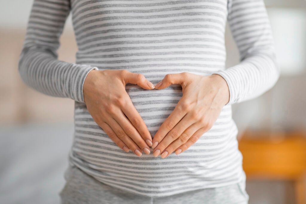 Close-up of a pregnant woman forming a heart shape with her hands on her striped shirt covering the belly