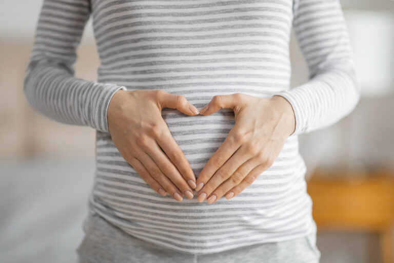 Close-up of a pregnant woman forming a heart shape with her hands on her striped shirt covering the belly