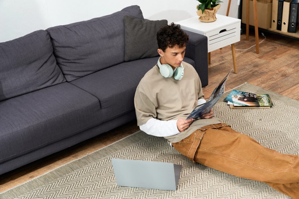 A teenager sits on the floor, reading a magazine and lost in his own world with headphones on.