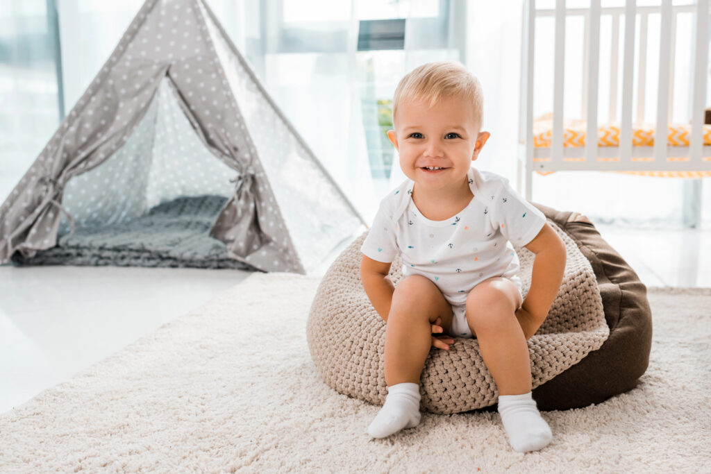 adorable smiling toddler sitting on bean bag chair and looking at camera in nursery room