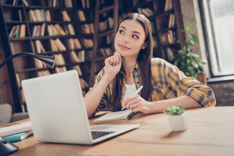 Portrait of attractive dreamy cheery girl learner doing home task using laptop fantasizing at loft industrial interior indoors