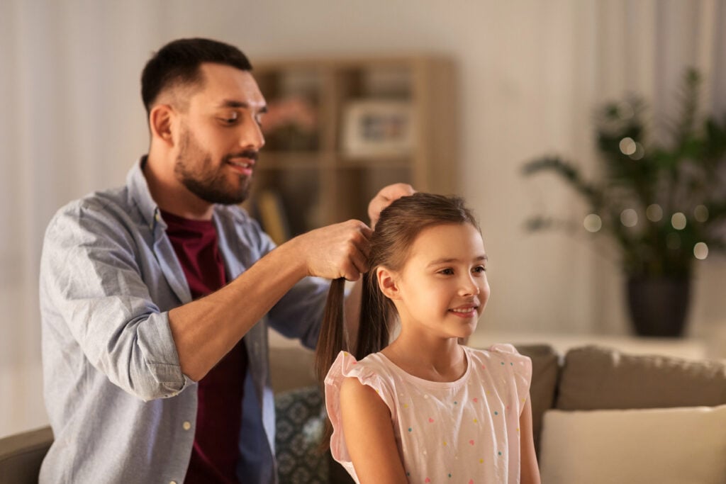 father braiding daughter hair at home