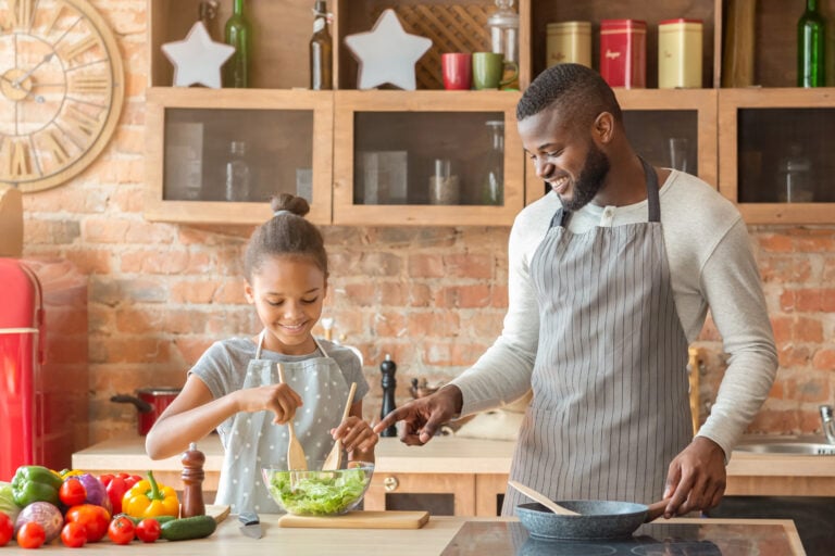 Cute girl mixing healthy veggies salad, father teaching her