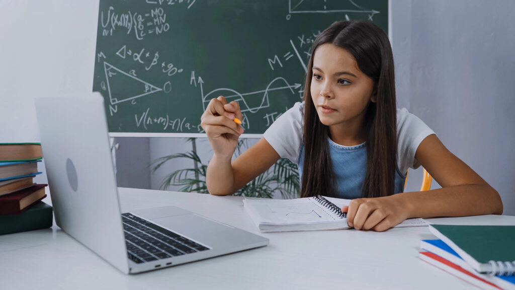 girl holding pen and looking at laptop while online studying at home