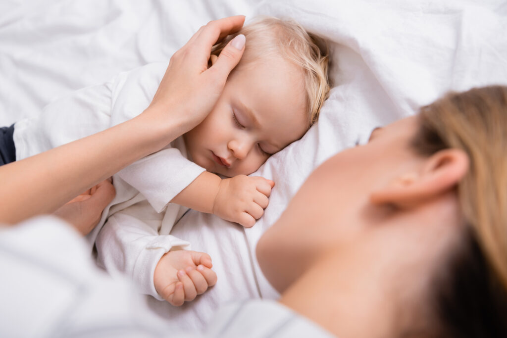 mother touching head of little son sleeping in bedroom, blurred foreground