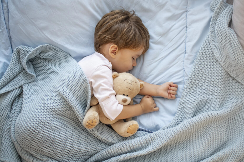 Photo of baby boy sleeping together with teddy bear. His favorite napping spot. Adorable kid boy after sleeping in bed with toy. Boy sleeping on bed with teddy bear. Sleepyhead